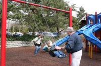 Grandpa Jim pushing Andrew and Mark on swings