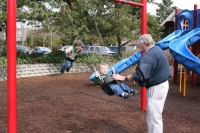 Grandpa Jim pushing Andrew and Mark on swings